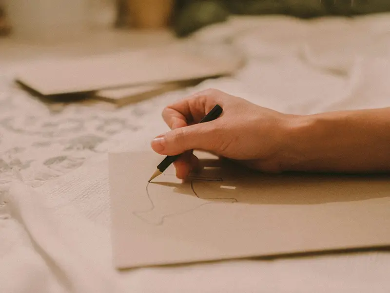 Une personne tient un crayon et dessine sur une feuille épaisse